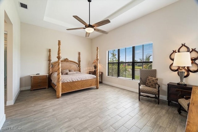 bedroom with visible vents, baseboards, a raised ceiling, ceiling fan, and light wood-type flooring