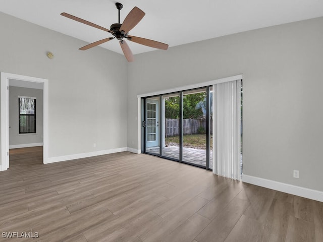 empty room featuring wood finished floors, high vaulted ceiling, baseboards, and a ceiling fan