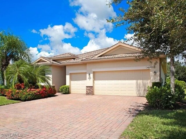 8143 Monticello Ct, Naples, FL 34104 - view of front of home featuring a tiled roof, stucco siding, decorative driveway, stone siding, and a garage