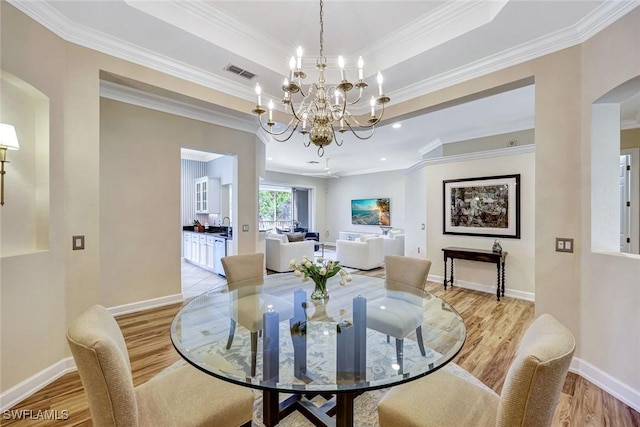 dining area featuring ornamental molding, light wood finished floors, an inviting chandelier, visible vents, and a raised ceiling
