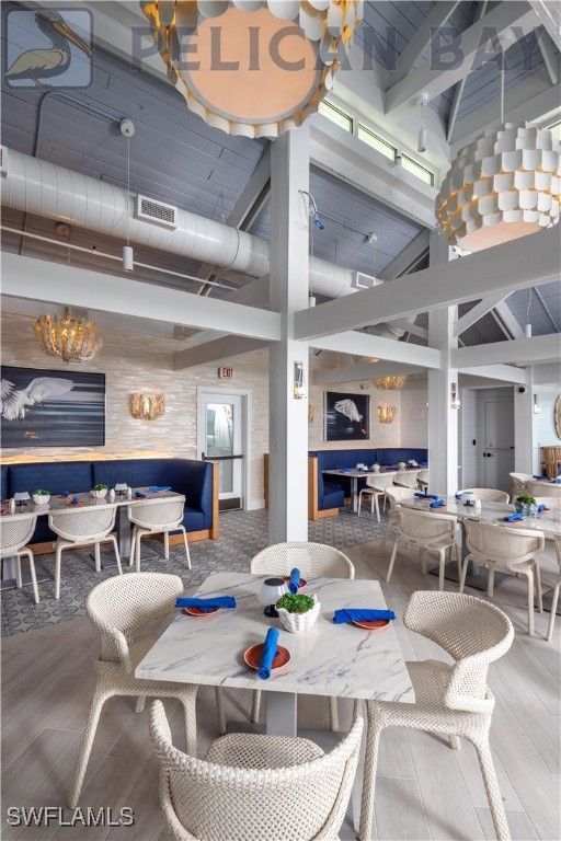 dining area with an inviting chandelier, a towering ceiling, visible vents, and wood finished floors