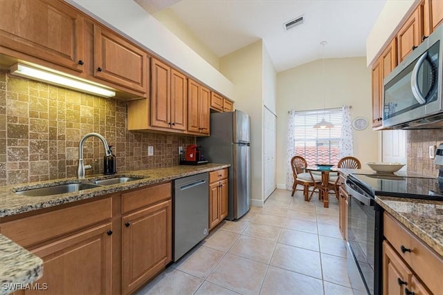 kitchen with a sink, brown cabinets, dark stone counters, stainless steel appliances, and light tile patterned flooring