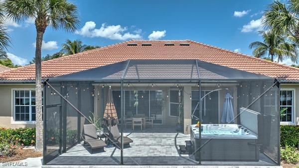 rear view of house with a patio, stucco siding, a lanai, a hot tub, and a tiled roof