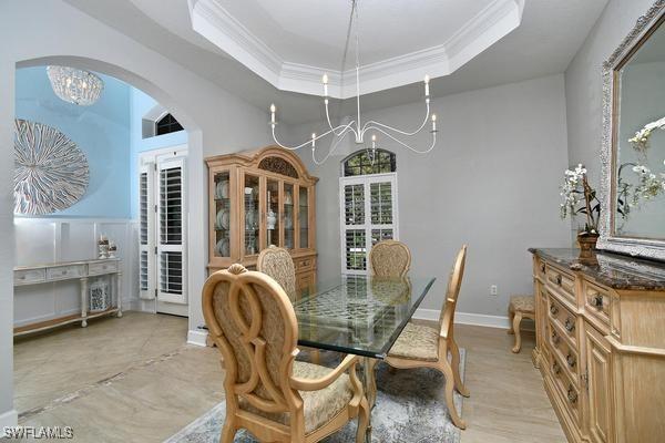 dining space featuring arched walkways, an inviting chandelier, crown molding, and a raised ceiling