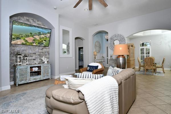 living room featuring arched walkways, light tile patterned flooring, baseboards, and a ceiling fan