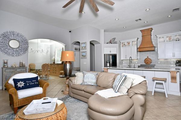 living area featuring arched walkways, visible vents, ceiling fan, and light tile patterned floors