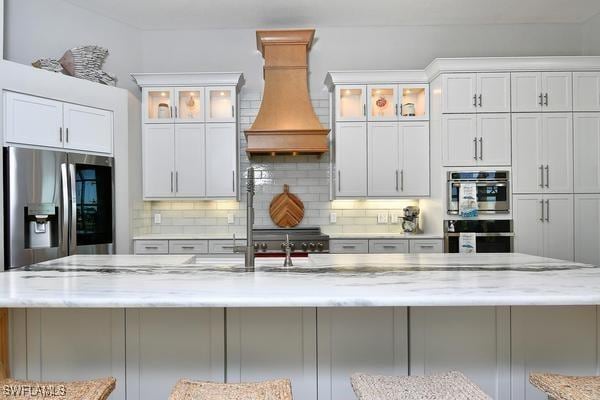 kitchen featuring stainless steel appliances, custom exhaust hood, tasteful backsplash, and a breakfast bar area
