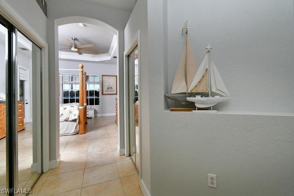 hall featuring a tray ceiling, arched walkways, light tile patterned floors, and baseboards