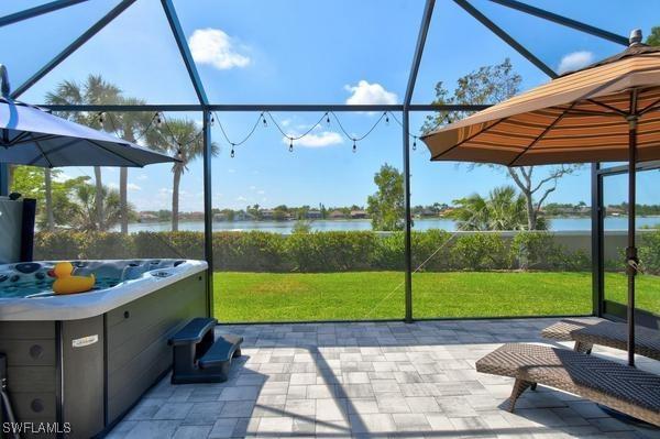 view of patio featuring a water view, glass enclosure, and a hot tub