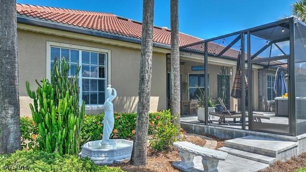rear view of house featuring a tile roof, glass enclosure, a patio, and stucco siding