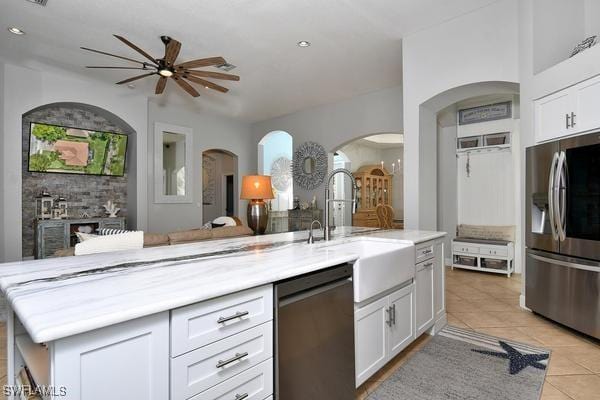 kitchen featuring light tile patterned floors, arched walkways, a sink, a ceiling fan, and stainless steel appliances