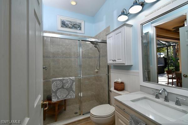 bathroom featuring toilet, a shower stall, vanity, and a wainscoted wall