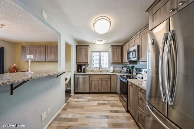 kitchen with appliances with stainless steel finishes, a sink, light stone counters, a kitchen breakfast bar, and a textured ceiling
