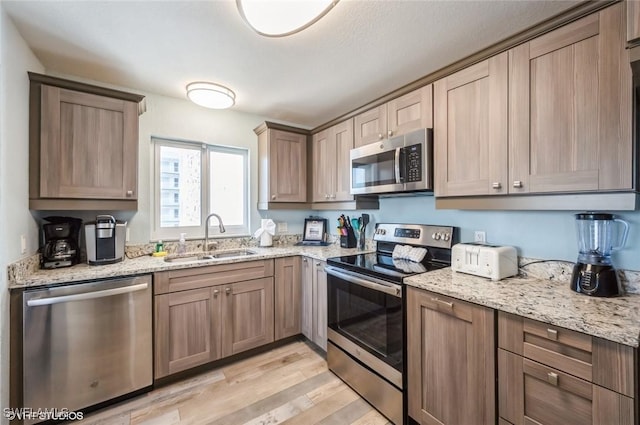 kitchen with stainless steel appliances, a sink, light wood-type flooring, and light stone counters