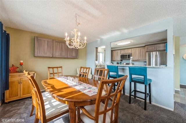 dining room featuring dark colored carpet, a chandelier, a textured ceiling, and baseboards