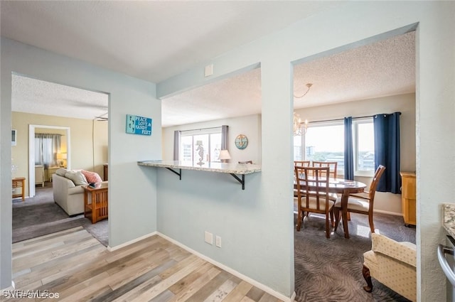 corridor featuring plenty of natural light, light wood-style floors, baseboards, a textured ceiling, and a chandelier