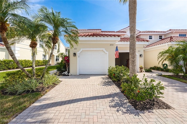 mediterranean / spanish-style home with an attached garage, stucco siding, a tile roof, and decorative driveway
