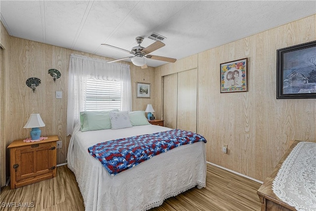 bedroom with wooden walls, visible vents, a closet, and wood finished floors