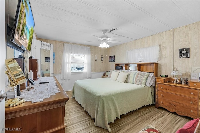 bedroom with wooden walls, visible vents, a ceiling fan, and wood finished floors