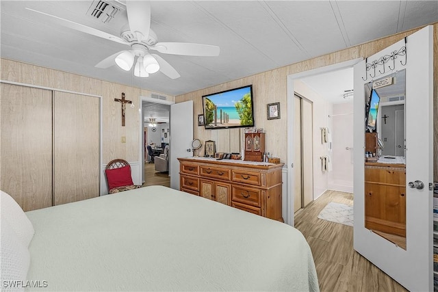 bedroom featuring a closet, ensuite bathroom, a ceiling fan, visible vents, and wood finished floors