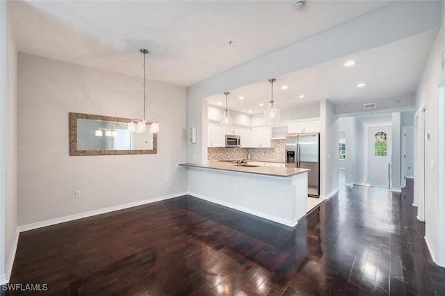 kitchen featuring decorative backsplash, white cabinets, appliances with stainless steel finishes, dark wood finished floors, and a peninsula