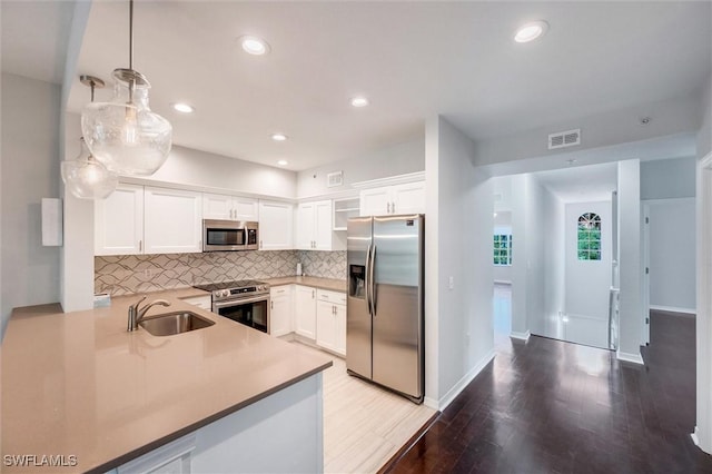 kitchen with white cabinets, a sink, stainless steel appliances, wood finished floors, and backsplash
