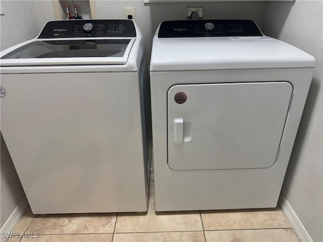 clothes washing area with baseboards, light tile patterned floors, separate washer and dryer, and laundry area