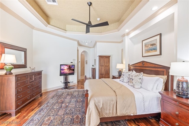 bedroom featuring ornamental molding, a tray ceiling, arched walkways, and wood finished floors