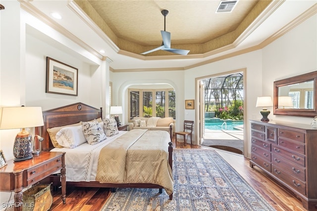bedroom with a tray ceiling, ornamental molding, visible vents, access to exterior, and wood finished floors