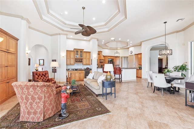 living room with crown molding, a raised ceiling, arched walkways, and ceiling fan with notable chandelier