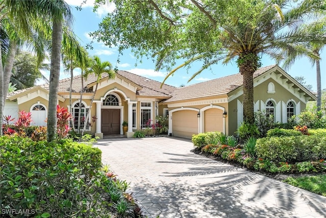 mediterranean / spanish-style home featuring an attached garage, a tiled roof, stucco siding, and decorative driveway
