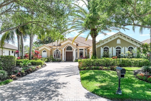 mediterranean / spanish-style home with stucco siding, a front yard, and decorative driveway