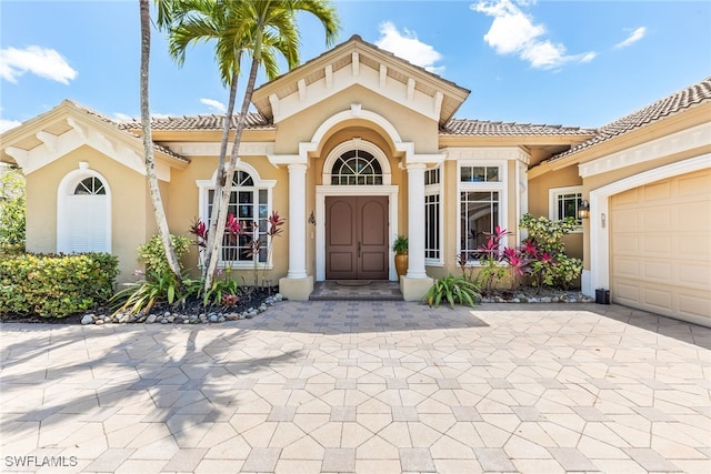property entrance with a tiled roof, decorative driveway, a garage, and stucco siding