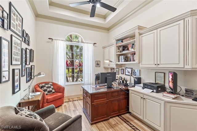 office area with light wood-style flooring, crown molding, a tray ceiling, and a ceiling fan