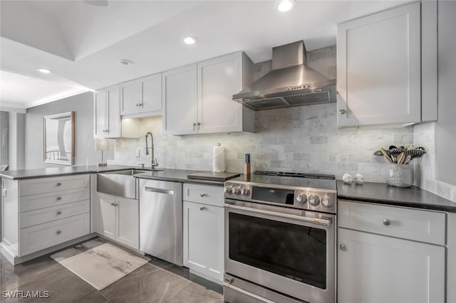 kitchen with a sink, wall chimney range hood, dark countertops, a peninsula, and stainless steel appliances