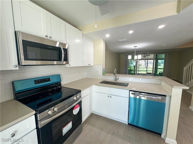 kitchen featuring appliances with stainless steel finishes, a sink, light countertops, a peninsula, and white cabinetry