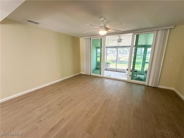 empty room featuring ceiling fan, a wall of windows, baseboards, wood finished floors, and visible vents