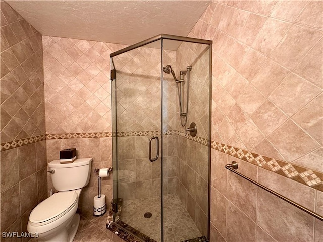 full bath featuring a textured ceiling, tile walls, tile patterned flooring, a stall shower, and toilet