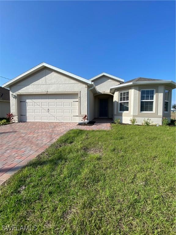 211 NE 20th St, Cape Coral, FL 33909 - ranch-style house with a front lawn, decorative driveway, a garage, and stucco siding