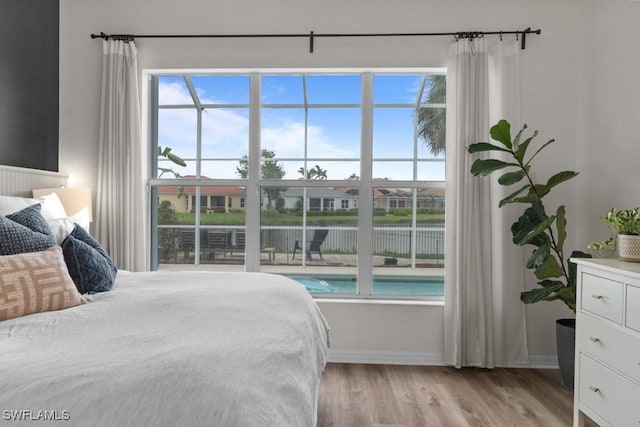 bedroom featuring baseboards, light wood-style floors, multiple windows, and a water view