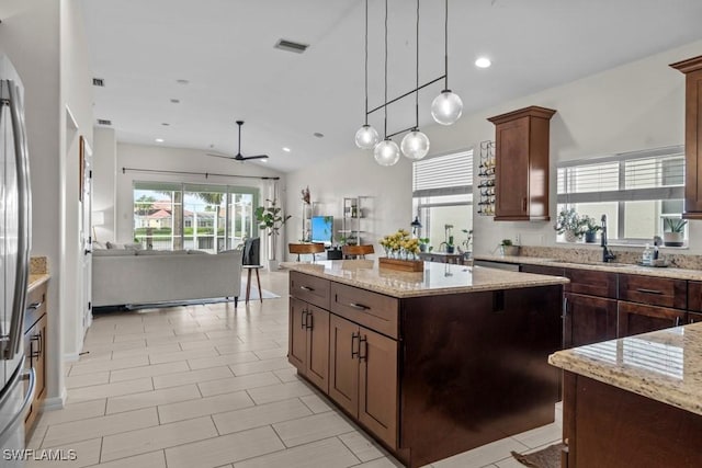 kitchen with a ceiling fan, a center island, a sink, pendant lighting, and light stone counters