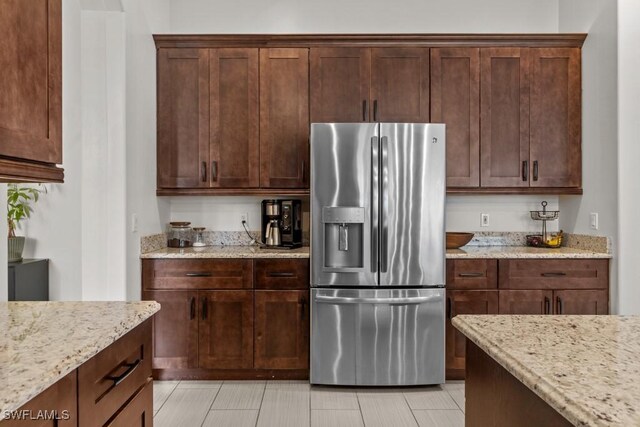 kitchen with stainless steel fridge with ice dispenser, light stone counters, light tile patterned flooring, and dark brown cabinets