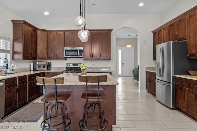 kitchen featuring appliances with stainless steel finishes, a sink, a kitchen island, arched walkways, and light stone countertops