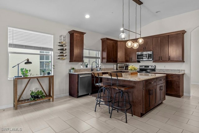 kitchen with appliances with stainless steel finishes, a center island, lofted ceiling, a kitchen breakfast bar, and dark brown cabinetry