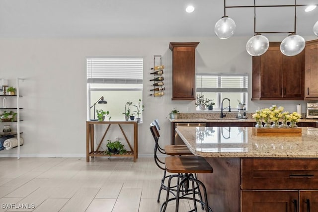 kitchen with a sink, a breakfast bar, light stone countertops, baseboards, and pendant lighting