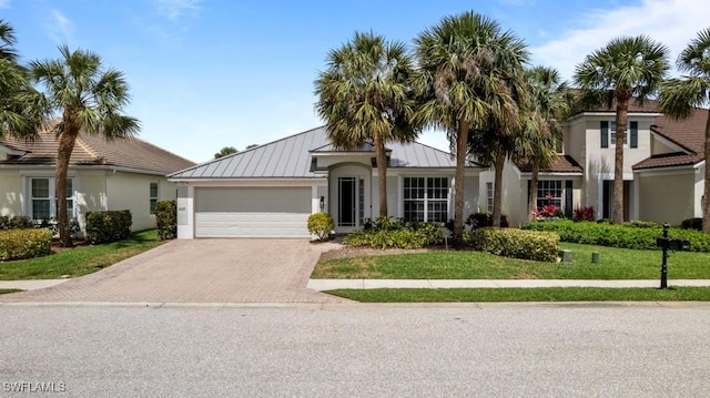 single story home featuring a standing seam roof, stucco siding, decorative driveway, an attached garage, and a front yard
