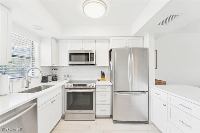 kitchen featuring appliances with stainless steel finishes, a sink, white cabinets, light countertops, and decorative backsplash