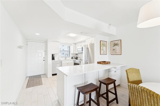 kitchen with appliances with stainless steel finishes, a peninsula, a sink, a kitchen breakfast bar, and white cabinetry