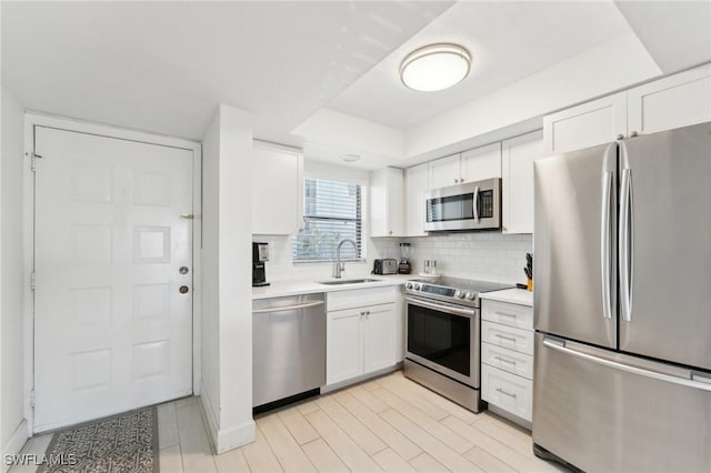 kitchen with stainless steel appliances, a sink, white cabinetry, and light countertops