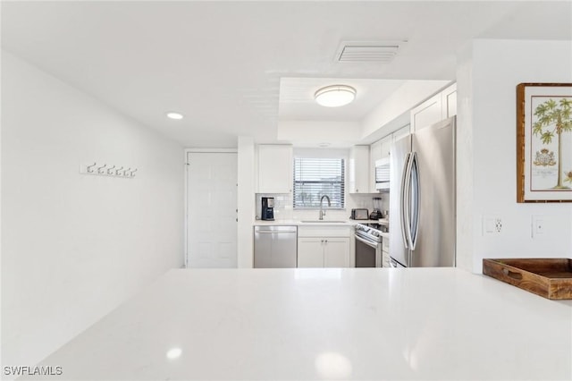 kitchen featuring appliances with stainless steel finishes, a sink, white cabinetry, light countertops, and tasteful backsplash